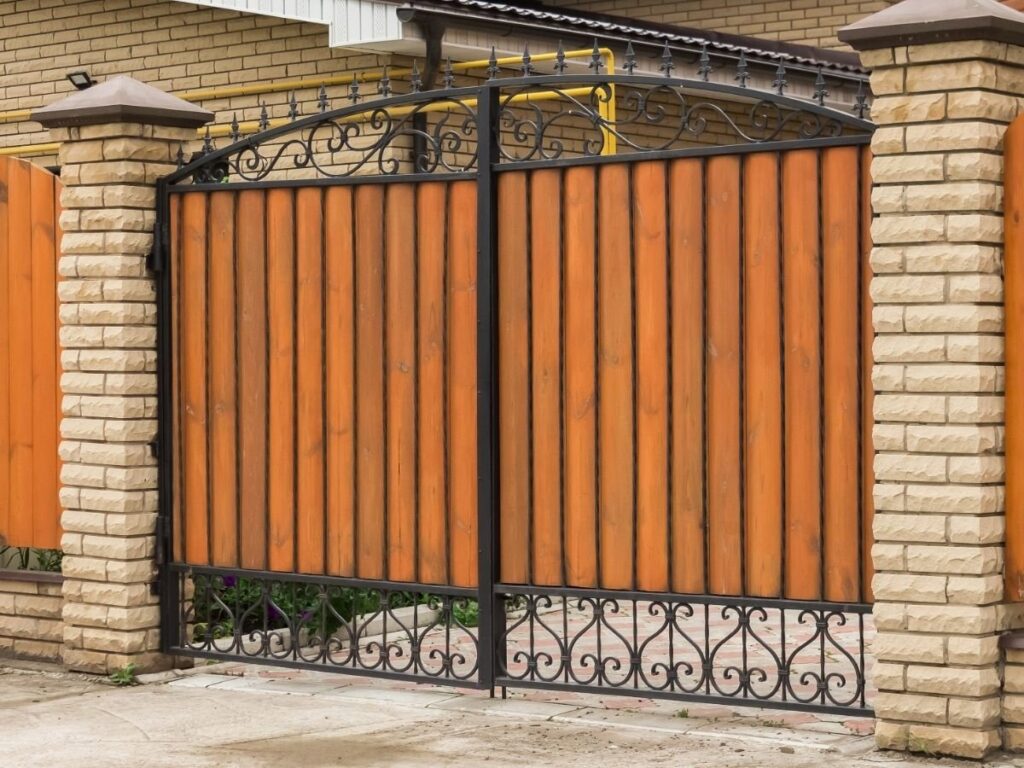 A sturdy wood and iron driveway gate with brick pillars, built by OneGuard Fencing in Vestavia Hills, AL.