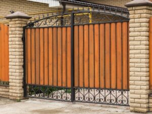 A sturdy wood and iron driveway gate with brick pillars, built by OneGuard Fencing in Vestavia Hills, AL.