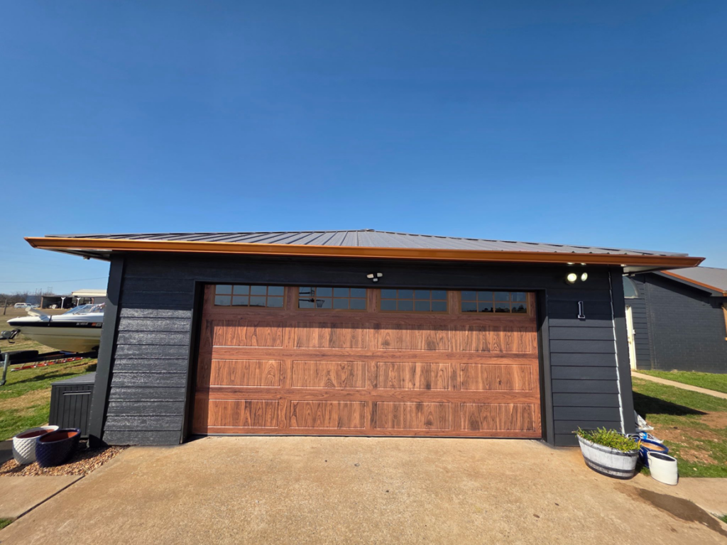 A newly installed wood-look garage door with windows on a dark-sided garage by APEX Garage Doors and Carports in Lawton, OK.