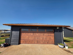 A newly installed wood-look garage door with windows on a dark-sided garage by APEX Garage Doors and Carports in Lawton, OK.