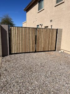 A wooden double gate with a black metal frame installed between two block walls by Competitive Fence Contractors LLC in Scottsdale, AZ.