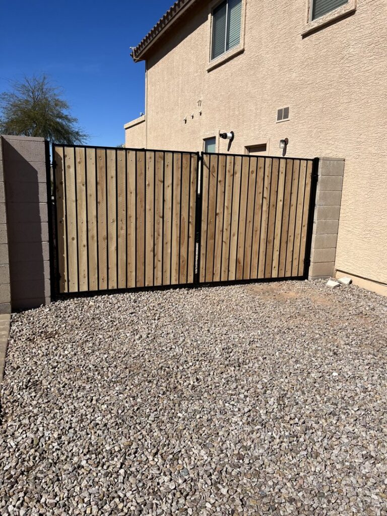 A wooden double gate with a black metal frame installed between two block walls by Competitive Fence Contractors LLC in Scottsdale, AZ.