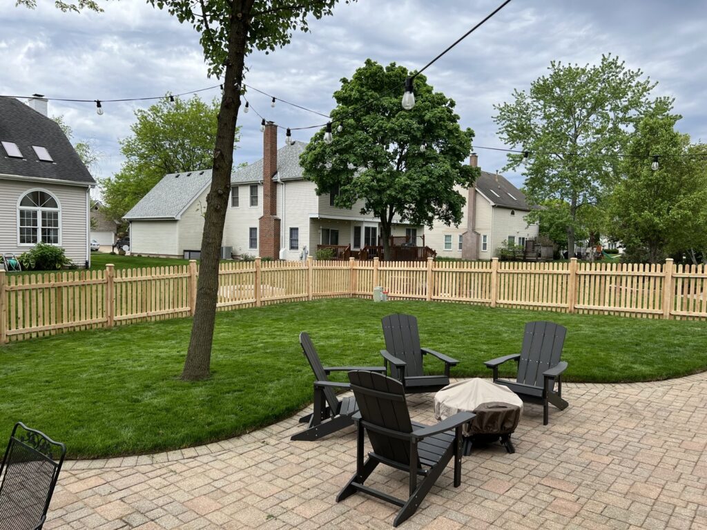 A wood picket fence enclosing a backyard with a patio by Cedar Mountain Fence Company in Plainfield, IL.