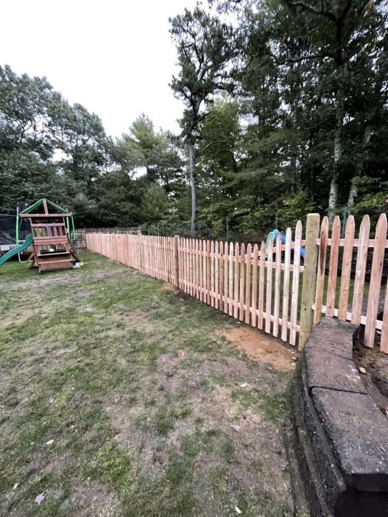 A new wooden picket fence installed in a backyard with a playset by OMA Fence,LLC in Weymouth, MA