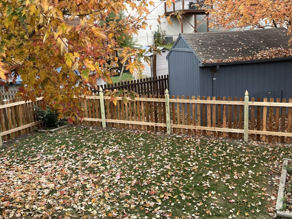 A newly installed wood picket fence with decorative post caps in a backyard by Sergio's Fence in Kansas City, KS.