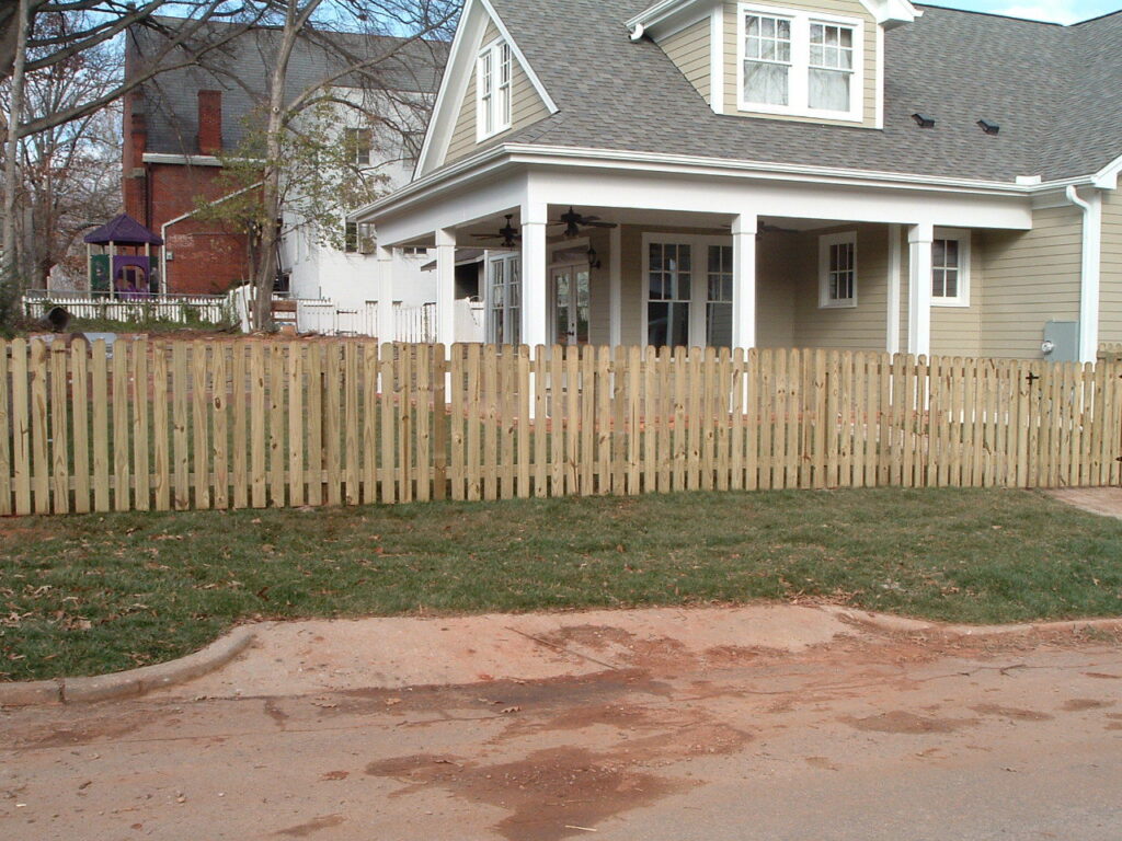 A classic wood picket fence installed in the front yard of a residential home by Endurance Fence Solutions, LLC in Holly Springs, NC
