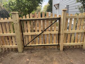 A sturdy wood picket fence with a gate reinforced by a metal frame, installed by Charleston Fencing Services in Moncks Corner, SC.