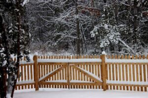 A charming wooden picket fence and gate covered in a fresh blanket of snow, installed by Sullivan & Sons Fence LLC in Hudson, NH.