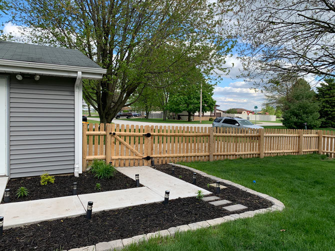 A natural wood picket fence with a gate installed next to a home by AmeriDream Fence & Deck in Joliet, IL.