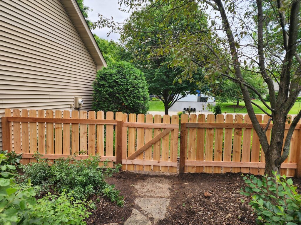 A newly installed wood picket fence with a matching gate next to a house by MN Mike's Fence and Repair in Lakeville, MN.