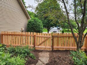 A newly installed wood picket fence with a matching gate next to a house by MN Mike's Fence and Repair in Lakeville, MN.