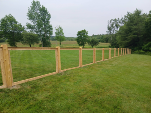 A long wooden post and wire mesh fence installed in a rural field by Creative Fence in Casco, ME.