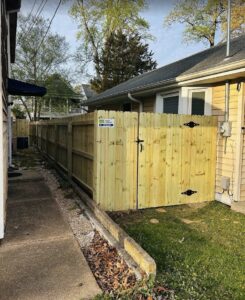 A newly installed wood privacy fence with a gate alongside a house, by Fast Fences LLC in Northfolk, VA.