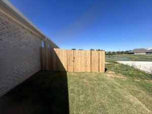 A new wood privacy fence and gate installed alongside a brick house by C & M Affordable Fence, LLC in Haughton, LA