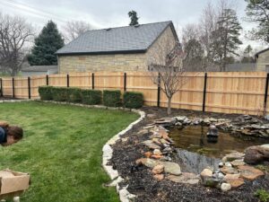 A wooden privacy fence with stylish black metal posts, enhancing a backyard with a pond, by Rio Fence Co. in Lincoln, NE.