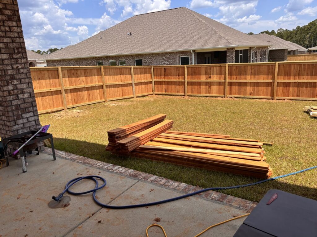 A wood privacy fence under construction with lumber stacked in a backyard by Deep South Services LLC in Biloxi, MS.