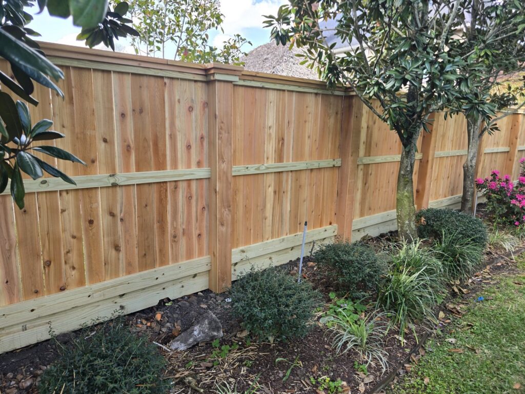 A new wood privacy fence with decorative top trim, enhancing a landscaped backyard, installed by Fence Builders of Houston, TX.