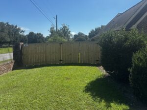 A custom wood privacy fence with a double gate next to a brick column, installed by FenceCo LLC in Pass Christian, MS.