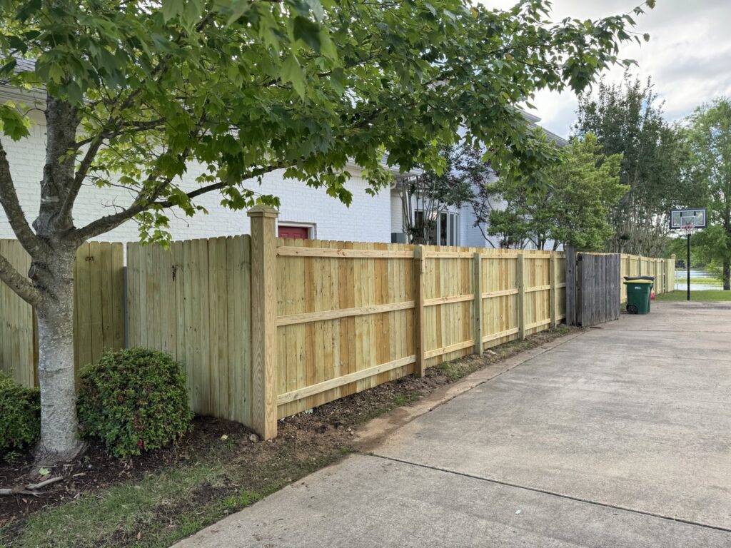 A newly installed wood privacy fence with a gate alongside a residential driveway by Faithful Fencing LLC in Batesville, AR.