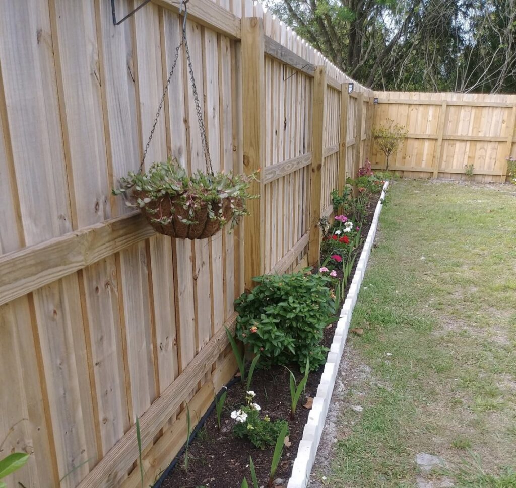 A charming wood privacy fence with a vibrant flower bed along its base, installed by Inovation Fence in Fort Worth, TX.