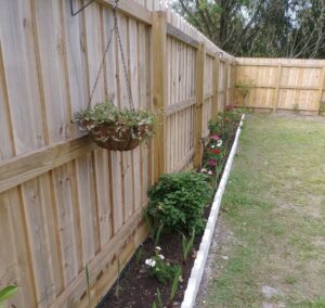 A charming wood privacy fence with a vibrant flower bed along its base, installed by Inovation Fence in Fort Worth, TX.