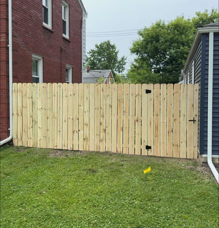 A newly installed wood privacy fence with a gate separating two properties by Final Touch Fencing LLC in Macomb Township, MI.