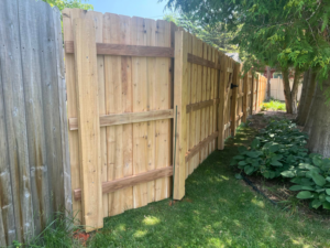 A long section of new wood privacy fence with a gate bordering a garden, installed by Northern Fence, Inc. in Appleton, WI.