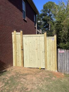 A newly installed wooden privacy fence gate next to a brick house by Jaguar Fence LLC in Mobile, AL.