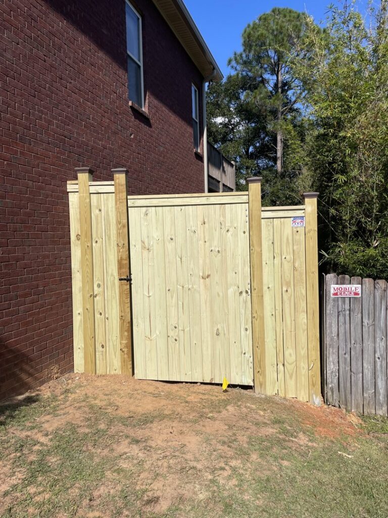 A newly installed wooden privacy fence gate next to a brick house by Jaguar Fence LLC in Mobile, AL.