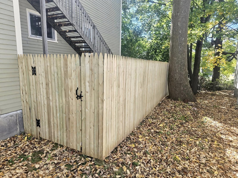 A newly installed wood privacy fence with a gate next to a residential building, completed by Dirigo Fence Company in Augusta, ME.