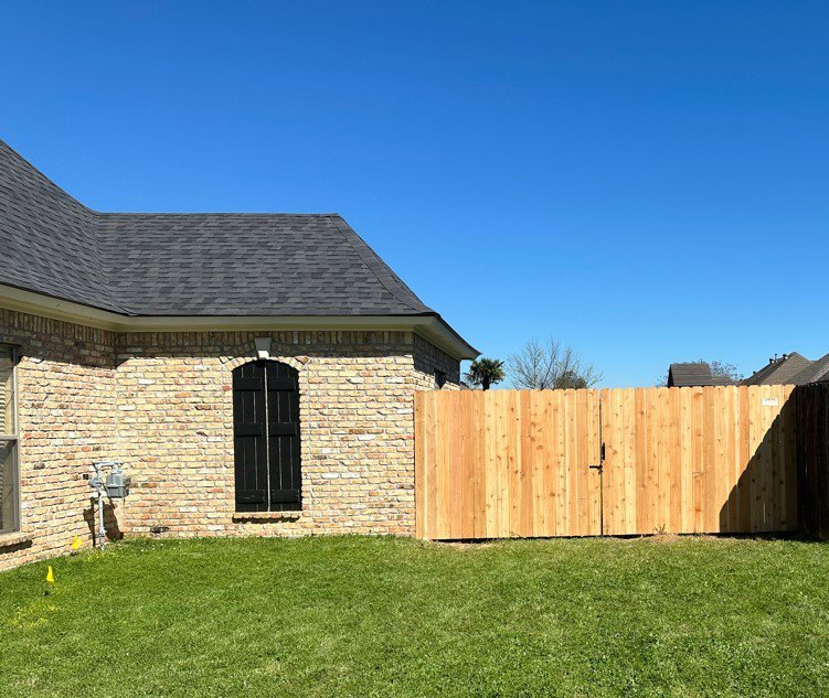 A new wood privacy fence with a gate installed next to a brick house by Lynch's Lawn & Fence LLC in Bossier City, LA.
