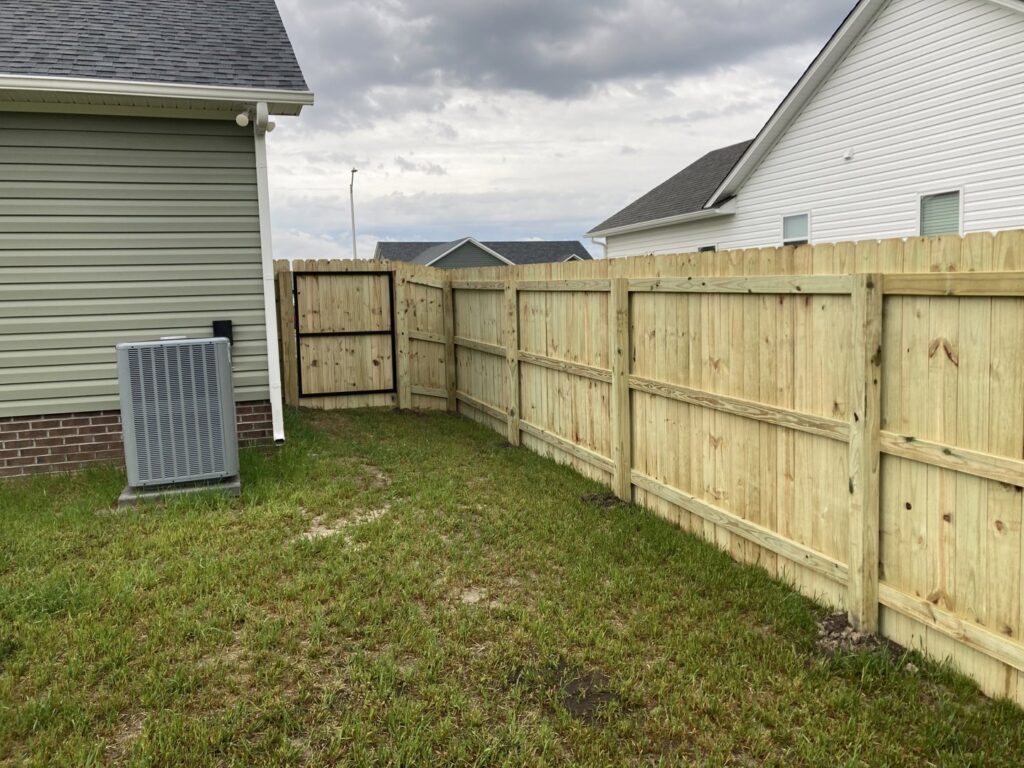 A wood privacy fence with a gate installed next to a residential home by Sea Level Fence in Harbinger, NC