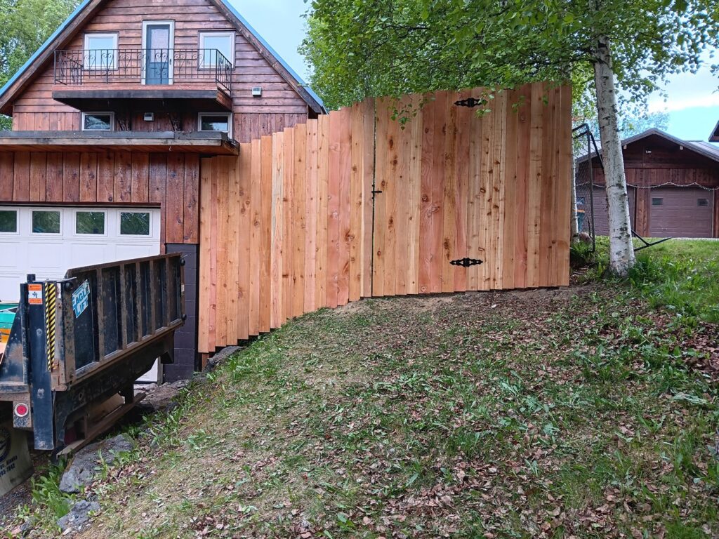 A new wood privacy fence with a gate installed on a sloped yard next to a house, by Five Star Fence Co. in Anchorage, AK.