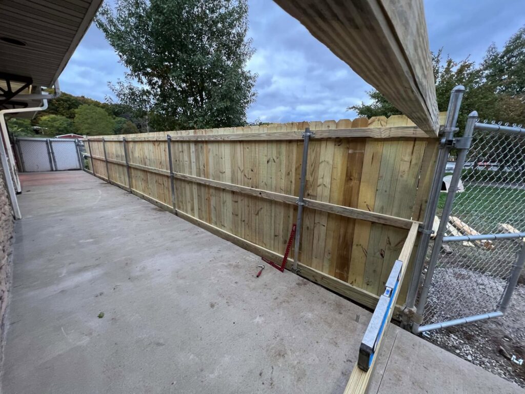 A new wood privacy fence being installed next to an existing chain-link fence by Camp Carlson Fencing in Rochester, NY.