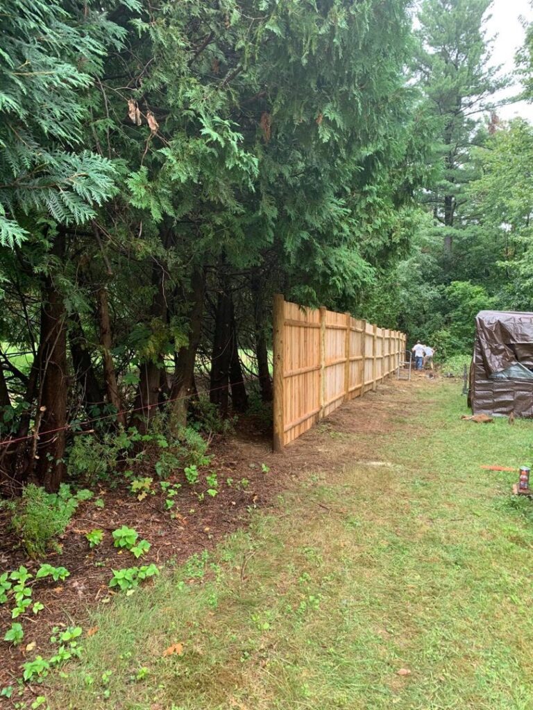 A wooden privacy fence installation in progress, showing a worker in the background, by Sullivan & Sons Fence LLC in Hudson, NH.