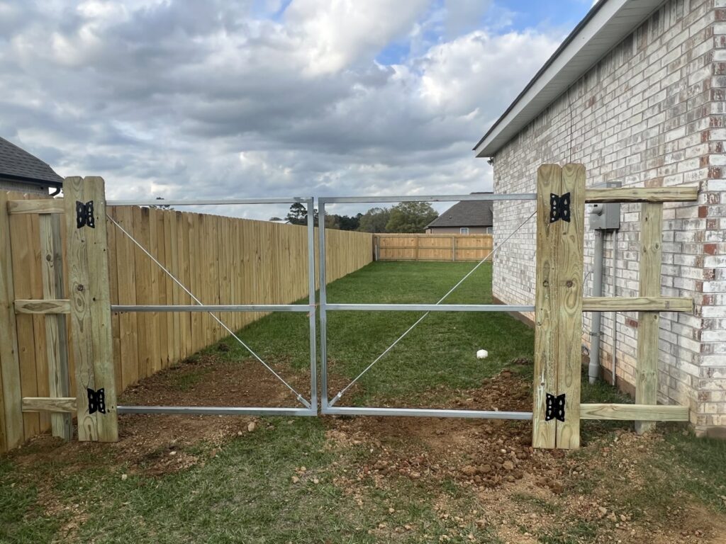 A wooden privacy fence with a metal frame double gate installed next to a brick residential home by Capitol Fencing in Baton Rouge, LA.