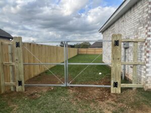 A wooden privacy fence with a metal frame double gate installed next to a brick residential home by Capitol Fencing in Baton Rouge, LA.