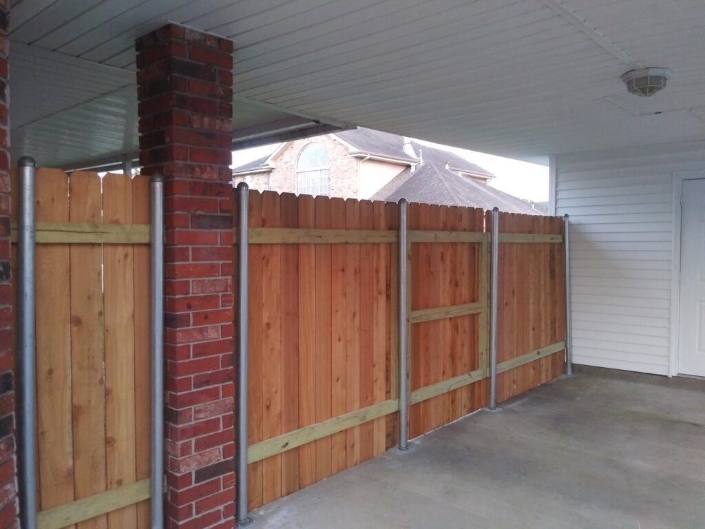 A custom wood privacy fence with sturdy metal posts integrated into a carport structure by Country Boyz fencing in Biloxi, MS.