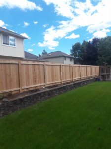 A wooden privacy fence installed on a stone retaining wall in a backyard by The Best Fence Company in Spokane, WA.
