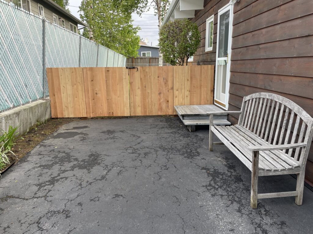 A new wood privacy fence installed alongside a paved area with a wooden bench, by Five Star Fence Co. in Anchorage, AK.