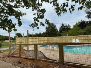 A new wood privacy fence with wire mesh sections being installed around a swimming pool area by 865 Fencing in Knoxville, TN.