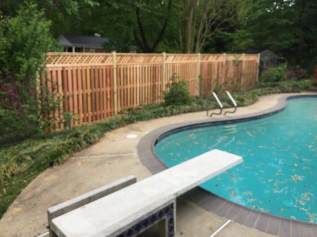 A wooden privacy fence with a decorative top installed next to a swimming pool by Universal Fence LLC in Drainesville, VA.