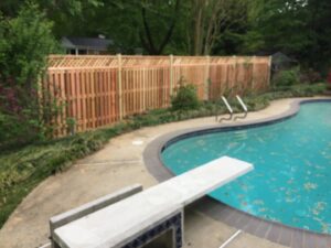 A wooden privacy fence with a decorative top installed next to a swimming pool by Universal Fence LLC in Drainesville, VA.
