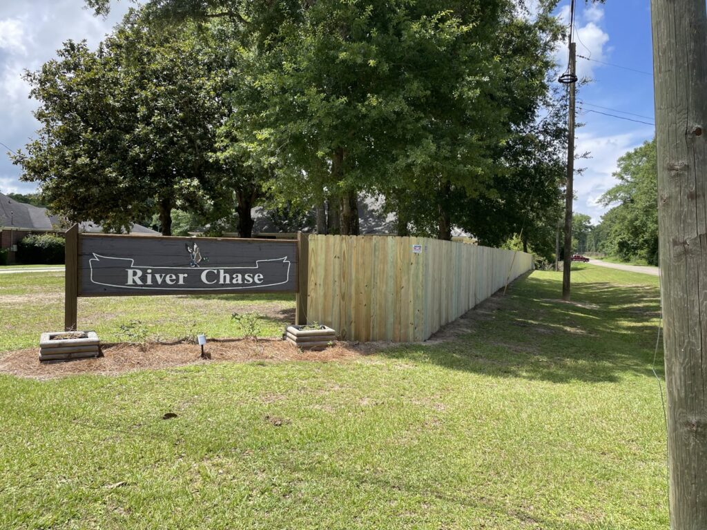 A long wooden privacy fence installed near a residential community entrance sign by Jaguar Fence LLC in Mobile, AL.