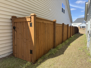 A wood privacy fence with a gate enclosing a side yard area next to a house, installed by Stain and Go in Summerville, SC.