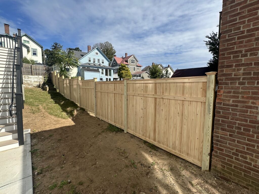 A long wooden privacy fence installed on a sloped residential property by Quality Fence Inc. in Peekskill, NY