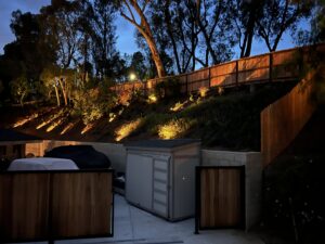 A wood privacy fence installed on a sloped backyard property, illuminated by landscape lighting by True American Fence Supply and Construction in Anaheim, CA.