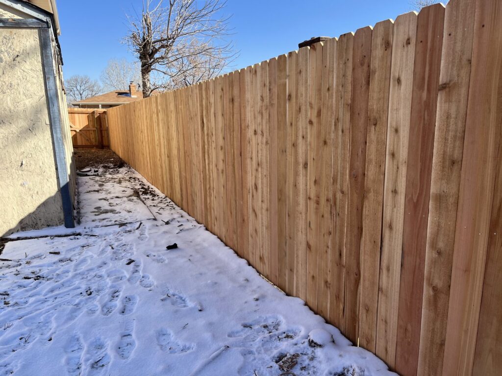 A newly installed wood privacy fence in a residential backyard with light snow by Supreme Fencing Denver, CO.