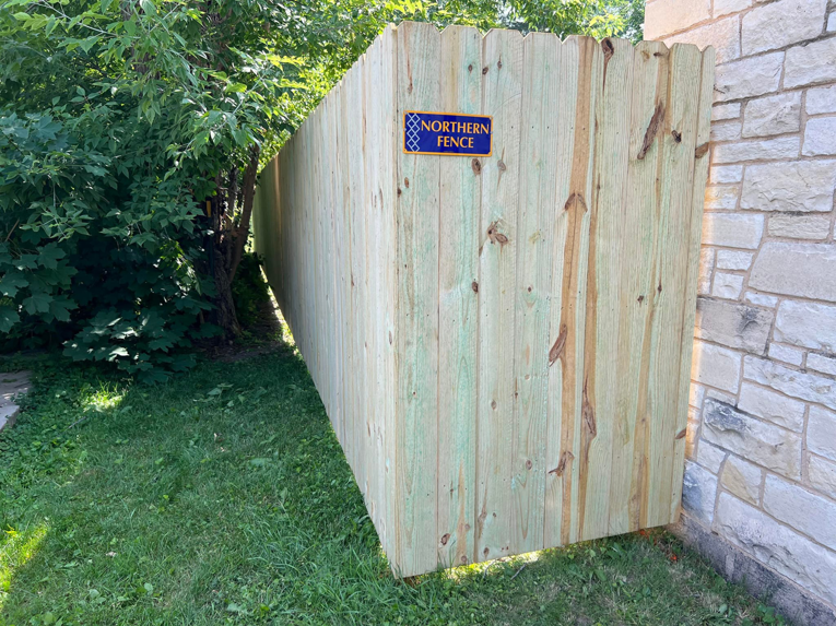 A newly installed wood privacy fence alongside a stone building by Northern Fence, Inc. in Appleton, WI.