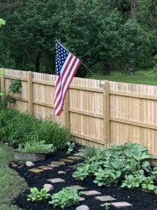 A newly installed wood privacy fence with an American flag attached, completed by City Fence Inc. in Lancaster, NY.